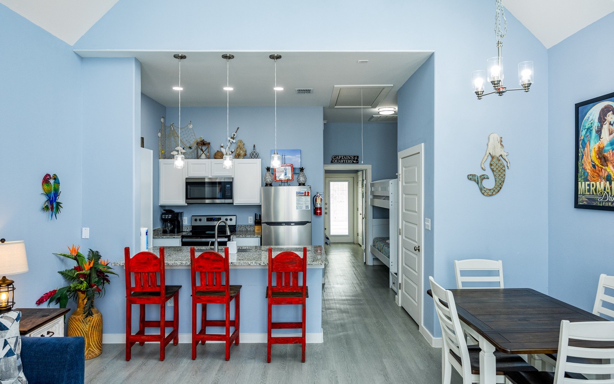Your coastal-themed open living space features a bright kitchen with granite countertops, vibrant red bar stools, and nautical decor.