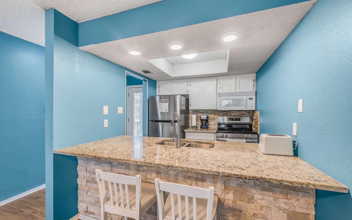 Cook your favorite meals in this bright, fully-equipped kitchen featuring granite countertops, stainless steel appliances, and cheerful coastal blue walls.