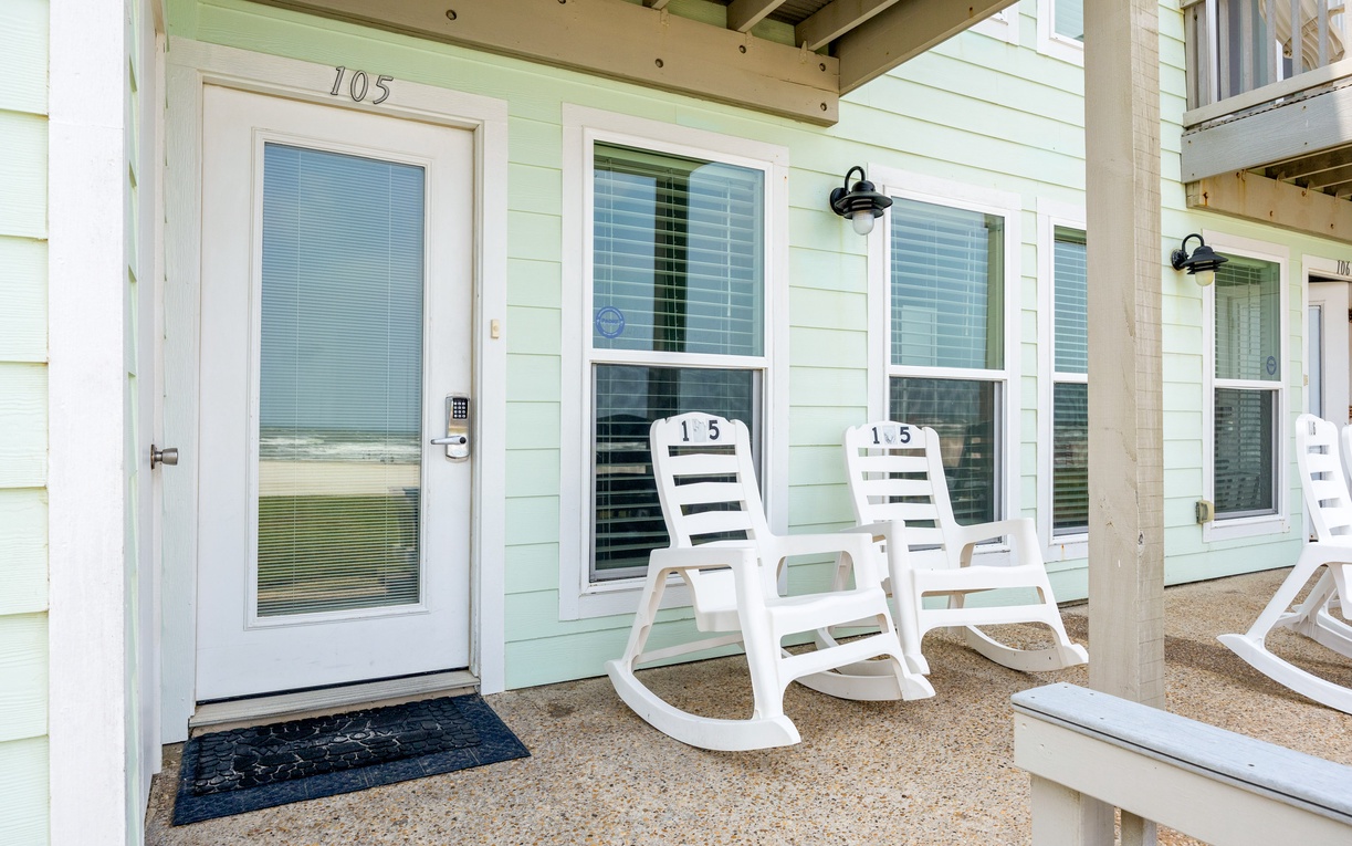 Charming seafoam-green cottage entrance with unit 105, featuring classic white rocking chairs on a welcoming covered porch for your relaxation.