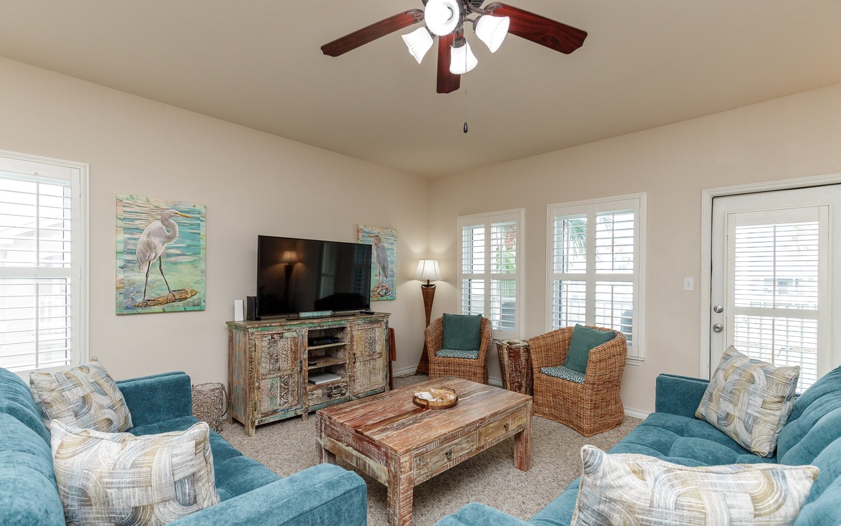 Relax in your coastal-themed living room with plush teal seating, tropical artwork, and entertainment center—perfect for unwinding after beach days.