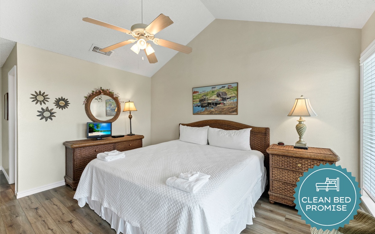 Relax in this peaceful bedroom with plush linens, soothing coastal artwork, and warm wicker furnishings that create your perfect retreat.