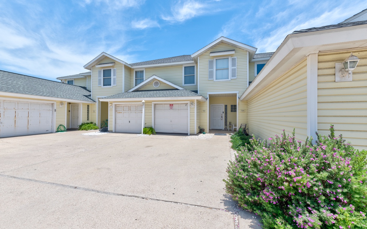 Charming two-story townhomes with private garages and blooming landscaping under clear blue skies.