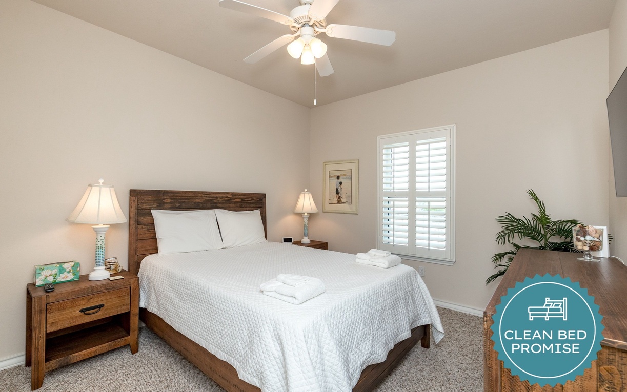 Unwind in your cozy bedroom featuring a comfortable bed, warm wood furnishings, and gentle ceiling fan for perfect relaxation.