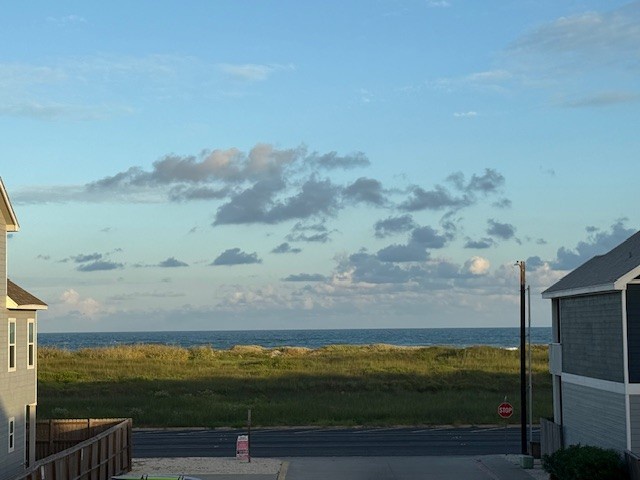Ocean views stretch beyond coastal dunes and grasses, with neighboring beach houses framing this peaceful seaside setting.