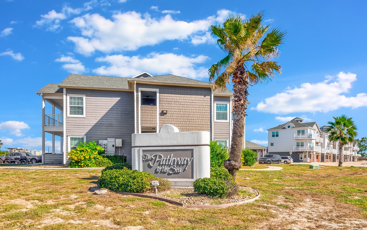 Charming coastal community entrance with palm trees and beachside homes creating a welcoming tropical atmosphere.