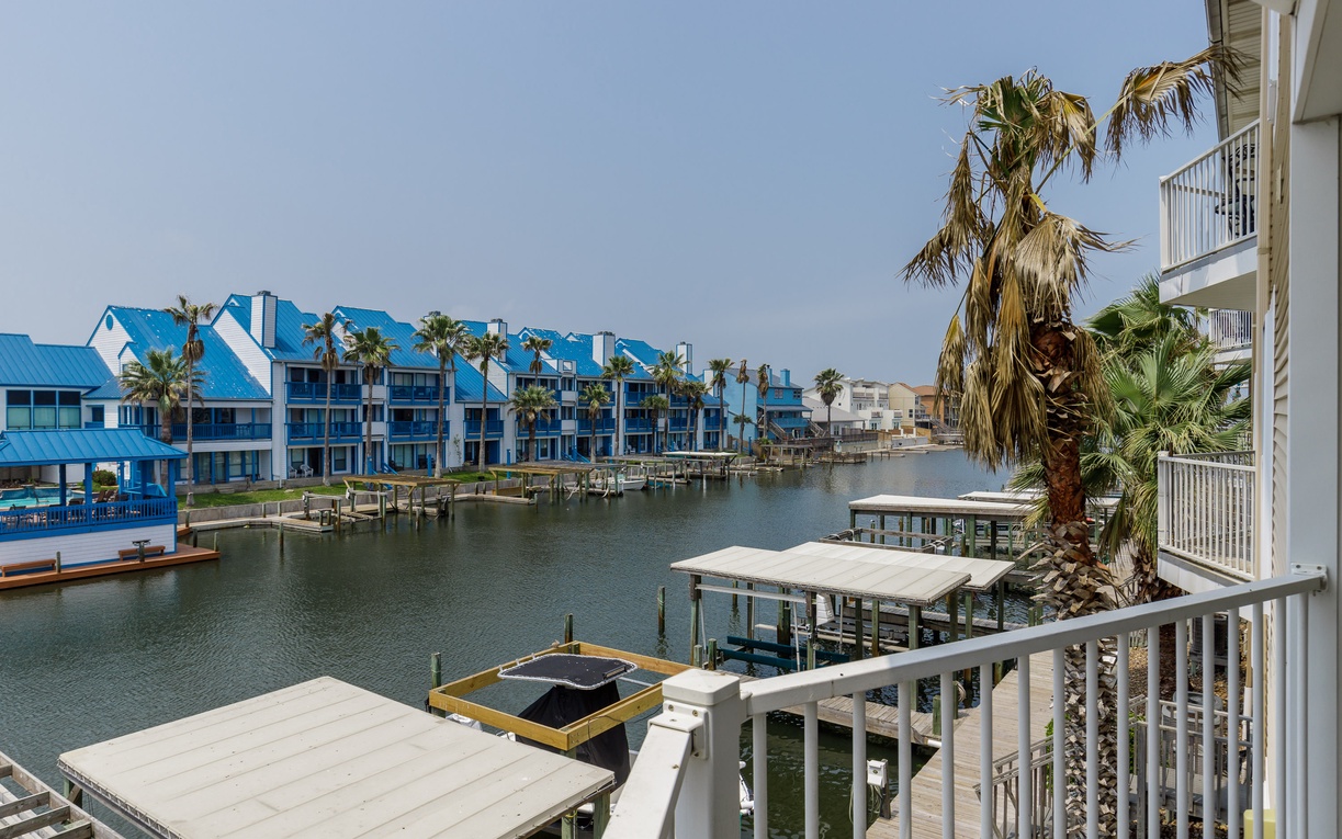 Waterfront balcony overlooking canal with colorful beach houses, private docks, and swaying palm trees in this tropical coastal community.