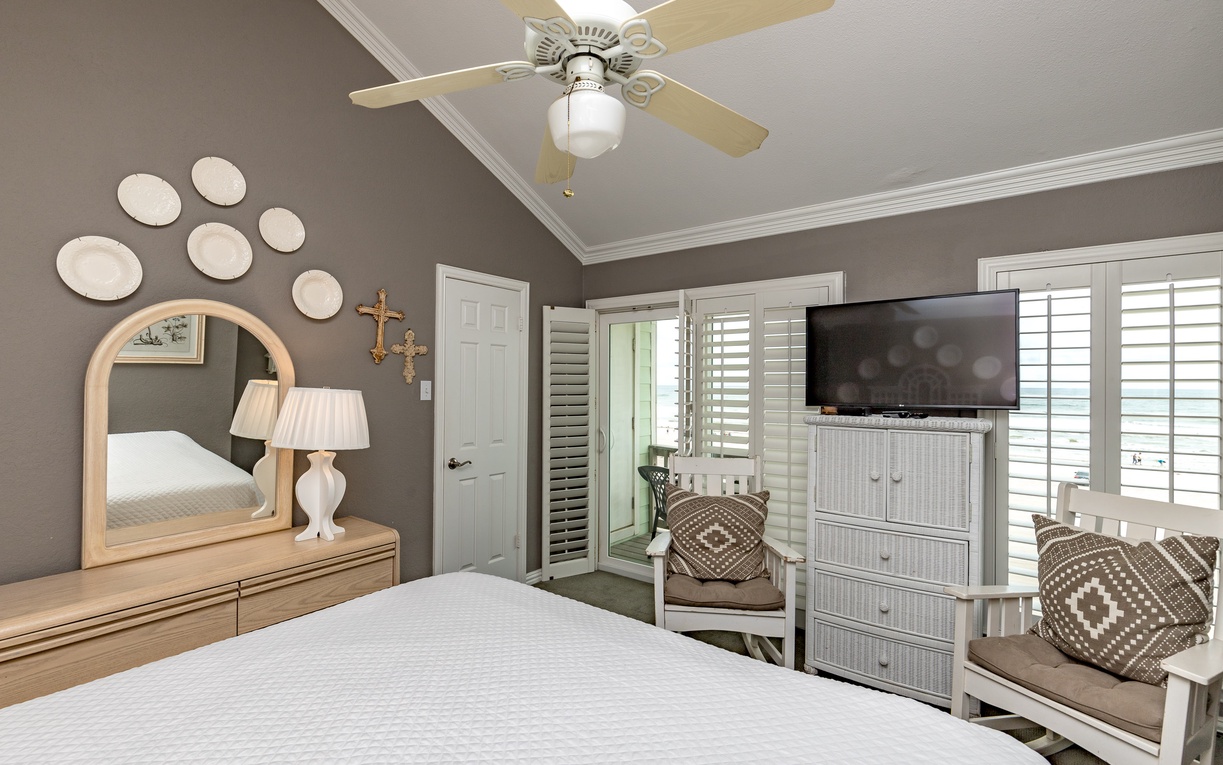 Relax in your beautifully appointed bedroom featuring coastal charm with crisp linens, soothing gray walls, and comfortable seating by the windows.
