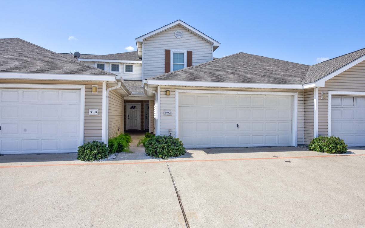 A charming two-story townhome with white siding, red shutters, and convenient garage parking in a peaceful residential community.