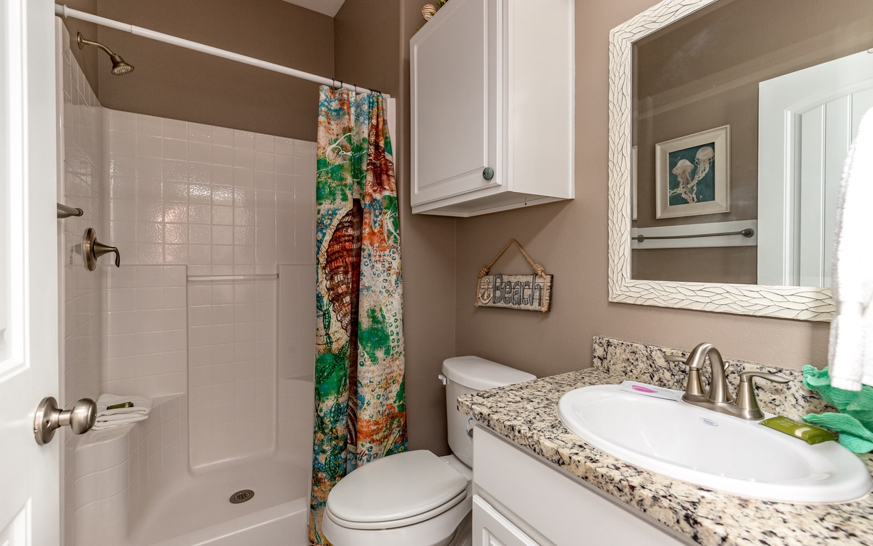 Step into your private bathroom featuring granite countertops, colorful beach-themed shower curtain, and coastal charm throughout.