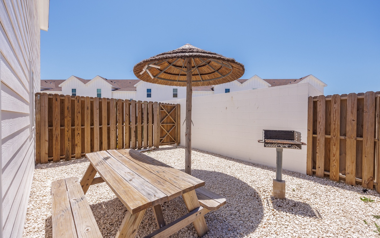 Your private outdoor oasis awaits with a shaded dining table, thatched umbrella, and BBQ grill perfect for sunny afternoon meals.