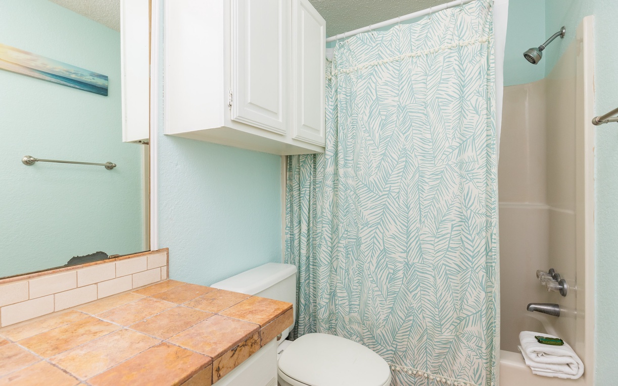 Step into your serene bathroom oasis with soothing mint walls, charming tile vanity, and tropical-patterned shower curtain creating coastal vibes.