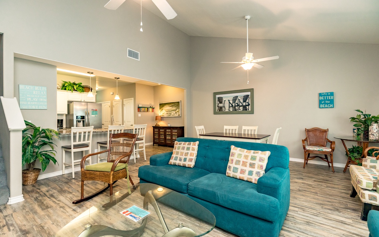 Relax in your spacious open-plan living area with vibrant turquoise sofa, modern kitchen, and coastal-themed touches throughout.