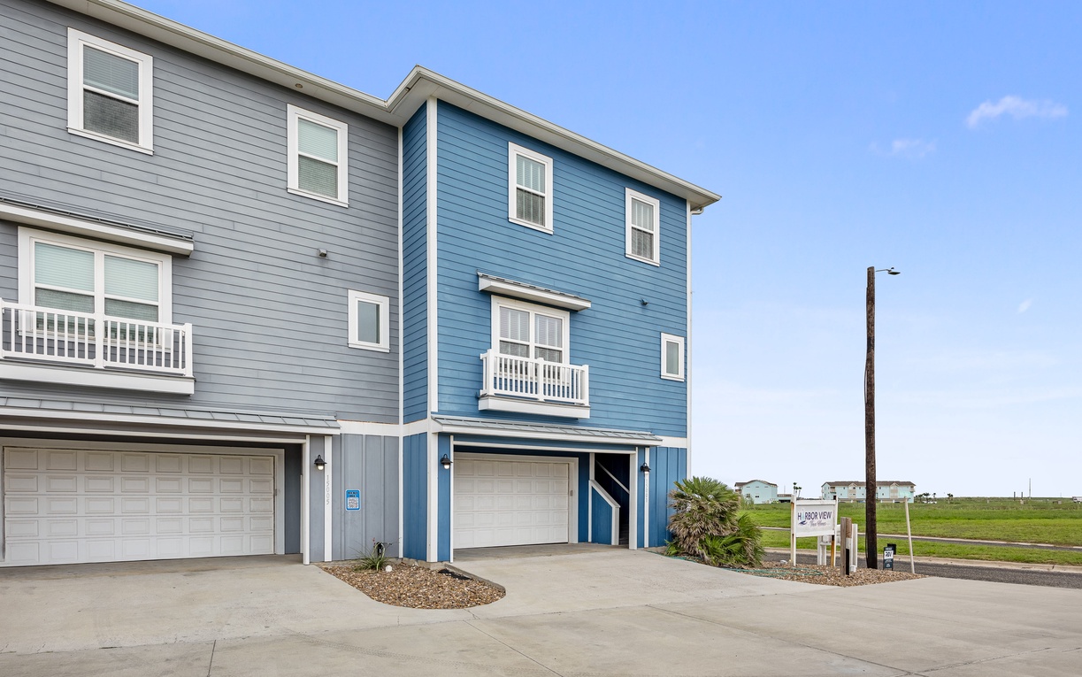 Modern coastal townhome with bright blue siding and garage parking in a peaceful residential development.