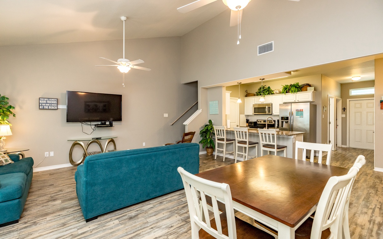 Relax in your spacious open-concept home featuring a bright living area with teal sofa and dining space flowing into a fully equipped kitchen.