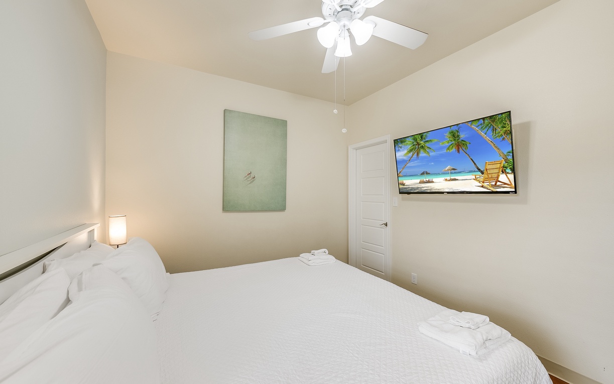 Rest peacefully in this serene bedroom with crisp linens, gentle ceiling fan breeze, and wall-mounted TV for your evening entertainment.