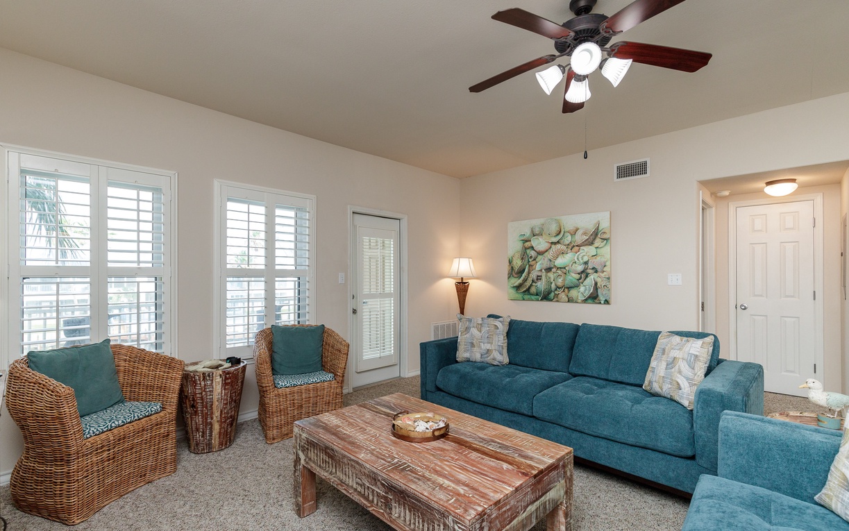 Relax in your coastal living room with teal furnishings, wicker accents, and plantation shutters creating the perfect beach getaway atmosphere.