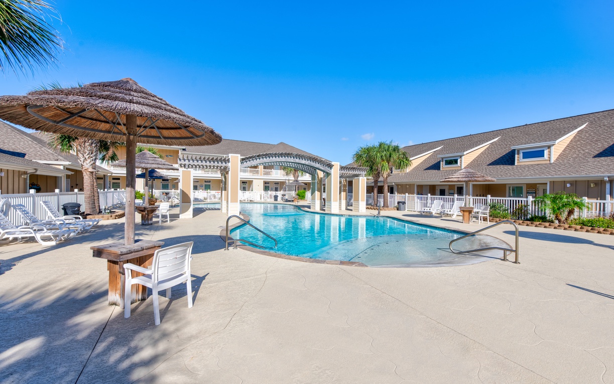 Sparkling pool area with tropical umbrellas and comfortable loungers surrounded by charming villa-style accommodations under endless blue skies.