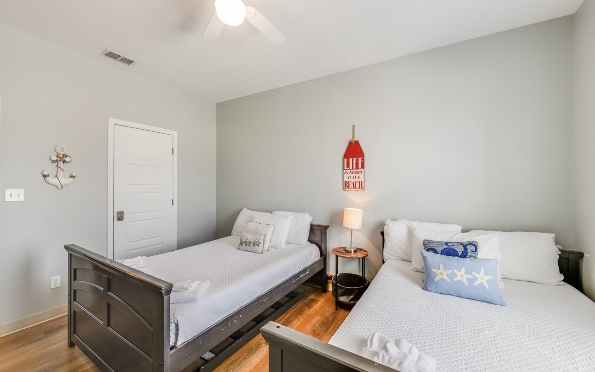 Unwind in your bright beach-themed bedroom with twin beds, coastal décor, and a relaxing ceiling fan for perfect comfort.