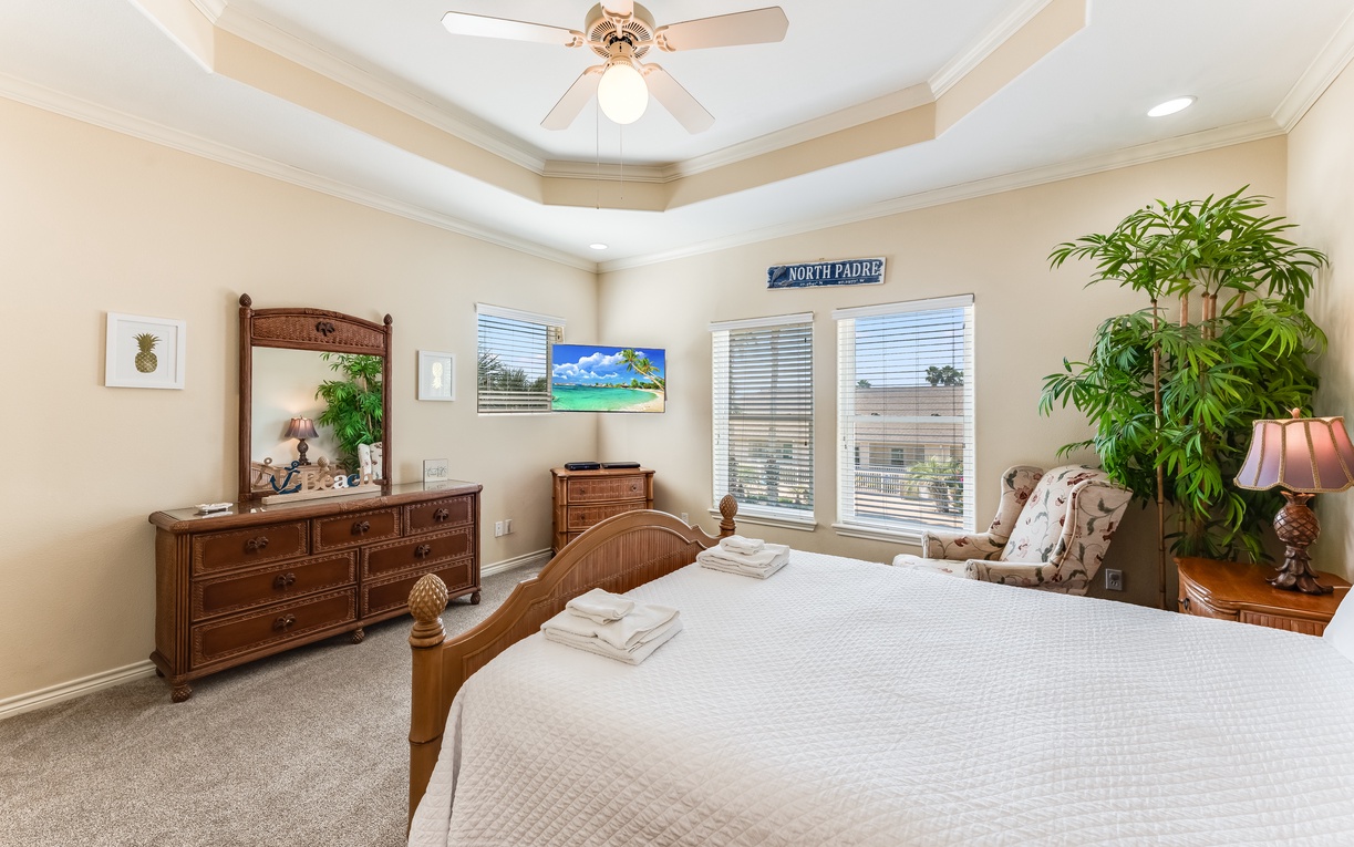 Unwind in your peaceful bedroom featuring tropical-inspired furniture, fresh towels, and natural light streaming through large windows.