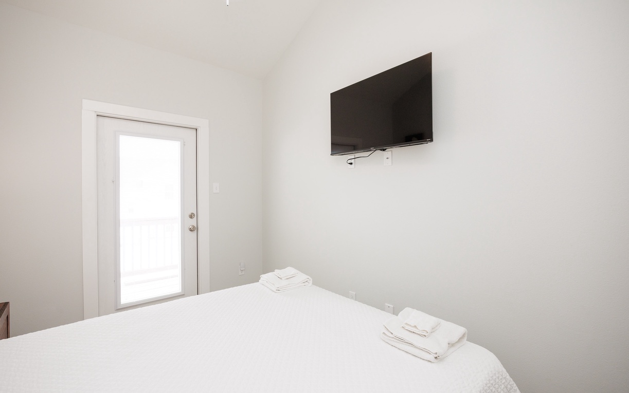 Your clean, minimalist bedroom offers crisp white linens and modern comfort with a wall-mounted TV for your evening entertainment.