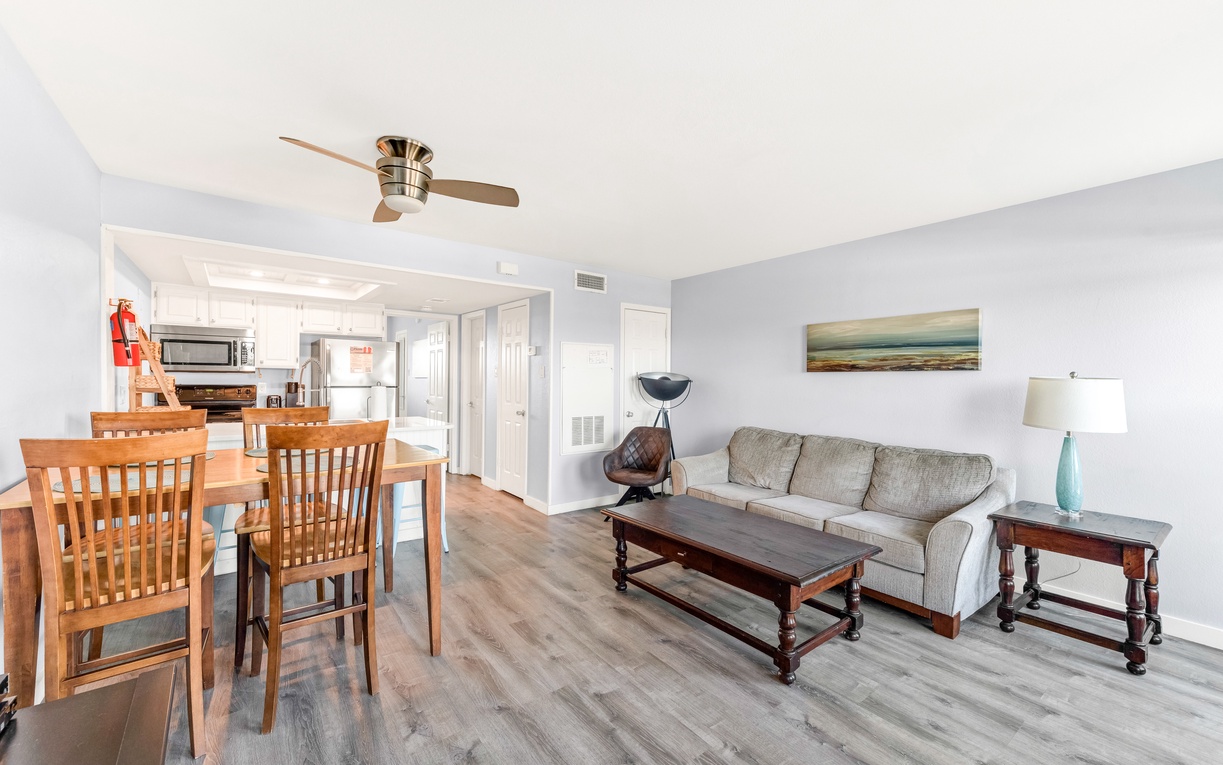 Relax in your bright, airy living space where modern comfort meets coastal charm, complete with ceiling fan and ocean artwork.