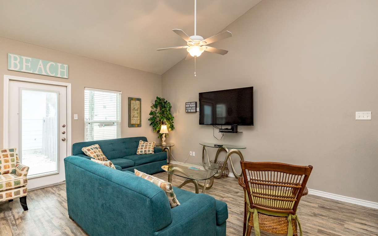 Relax in your bright living room with coastal vibes, comfortable teal seating, and entertainment center for cozy evenings.