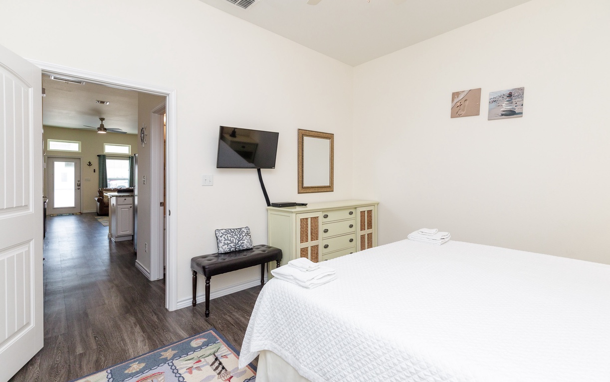 Relax in your serene bedroom with crisp linens, wall-mounted TV, and charming dresser.