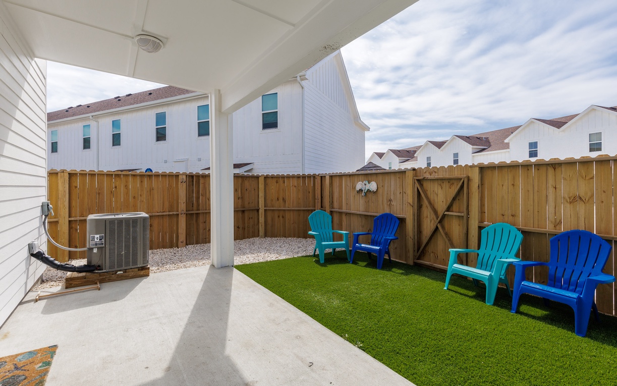 Your private backyard oasis awaits with vibrant Adirondack chairs on lush artificial turf, perfect for morning coffee or evening relaxation.
