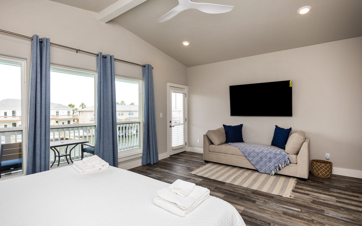 Unwind in your bright, airy bedroom featuring a cozy sofa, large TV, and private balcony access for peaceful moments.