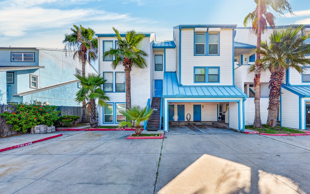 Welcome to your coastal getaway! This charming condo features cheerful blue accents, tropical palm trees, and convenient parking, setting the scene for a memorable beach vacation.