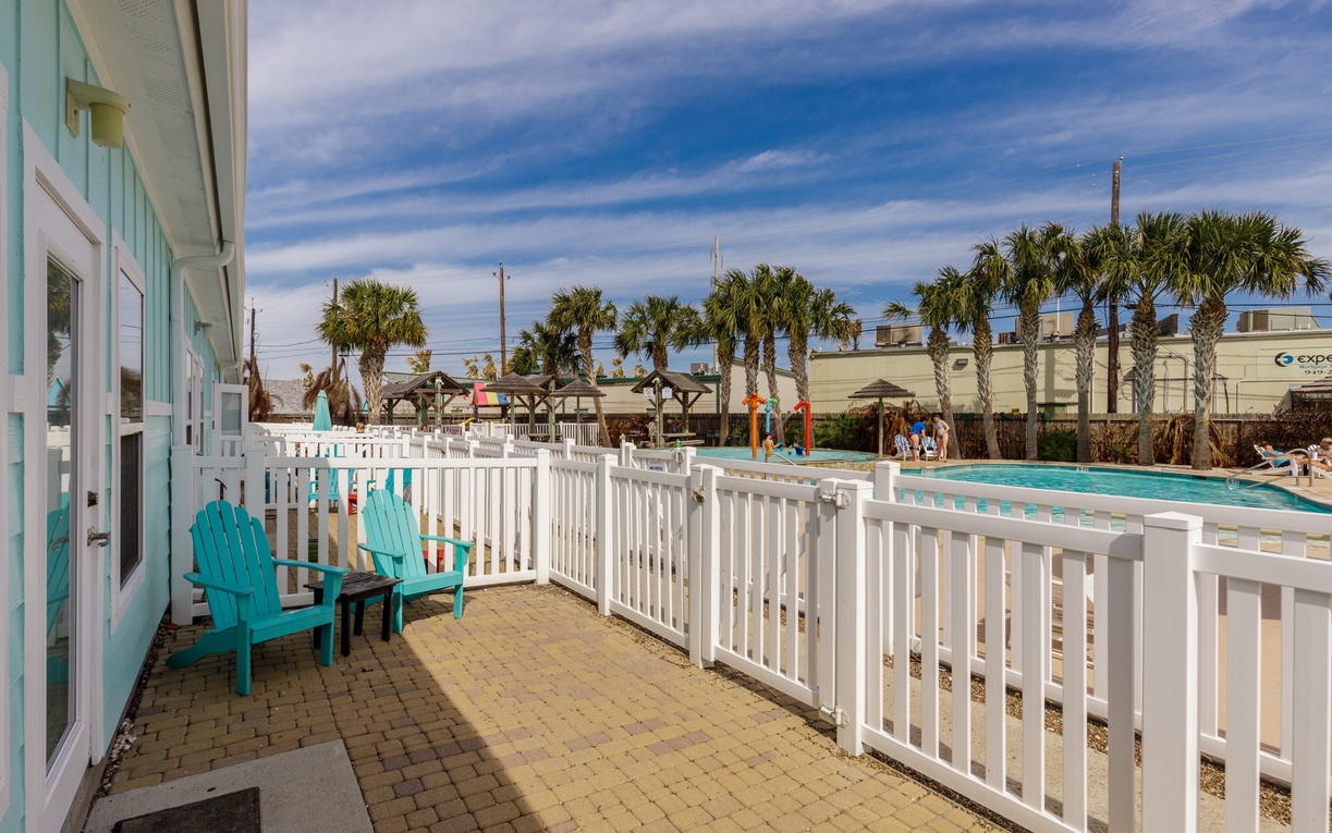 Your private patio features turquoise chairs overlooking the sparkling pool, where palm trees sway under endless blue skies.