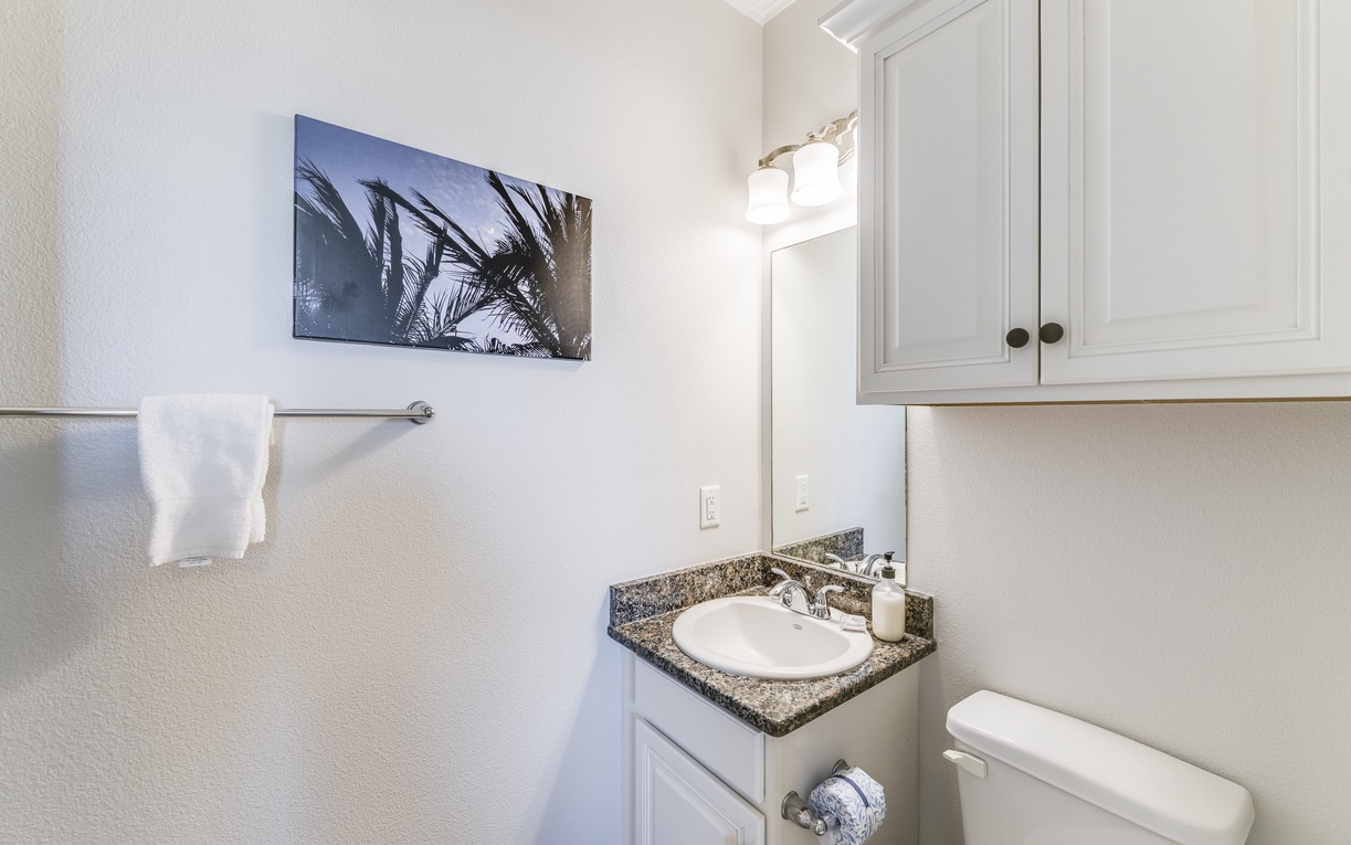 Step into your bright, well-appointed bathroom featuring granite countertops, crisp white cabinetry, and tropical artwork to set a relaxing mood.