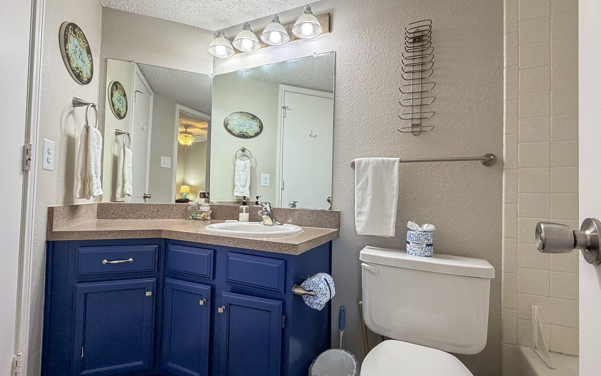 Refresh in your private bathroom featuring bright vanity lighting, rich blue cabinetry, and fresh towels ready for your stay.