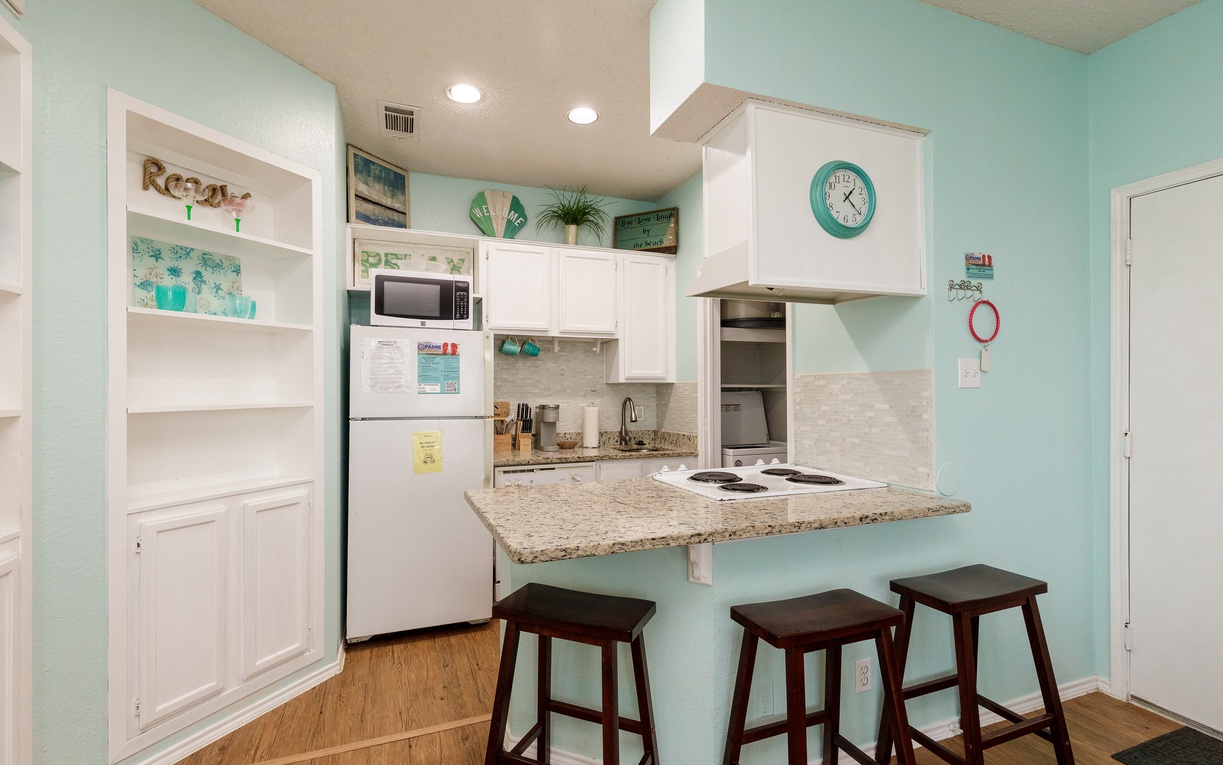 Your bright beachside kitchen invites morning coffee prep with granite counters, modern appliances, and cheerful coastal colors creating the perfect vacation vibe.