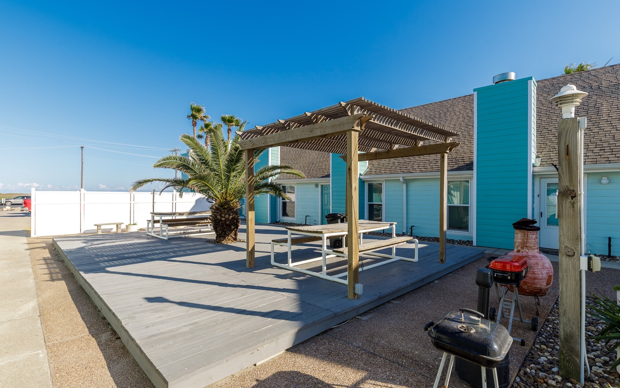 Waterfront complex with expansive, community patio featuring pergola-covered dining area, BBQ facilities, and tropical landscaping.