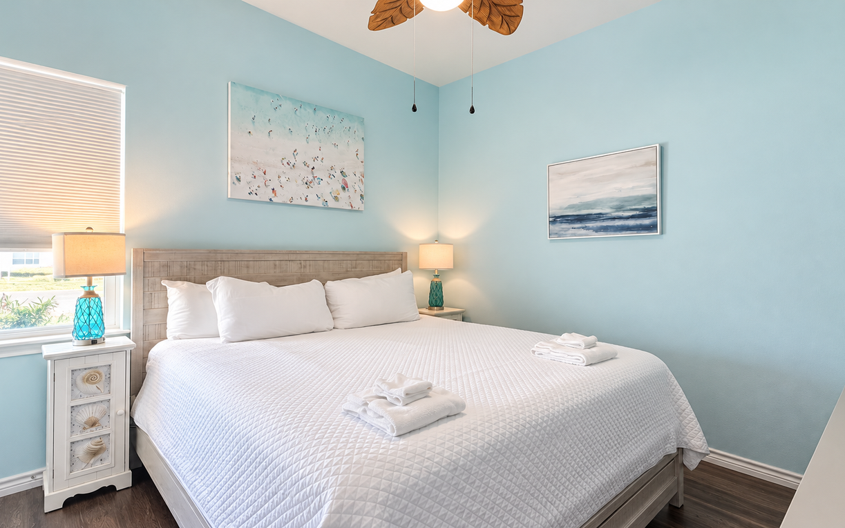 Step into your serene coastal escape, where soft blue walls and crisp linens invite you to unwind. Fresh towels await, and the palm-blade fan overhead keeps the breeze gentle and cool.
