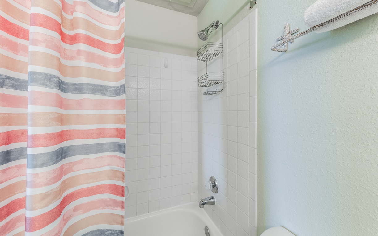 Step into your bright bathroom featuring a full tub-shower combo with cheerful coral striped curtain and handy shower caddy for your essentials.
