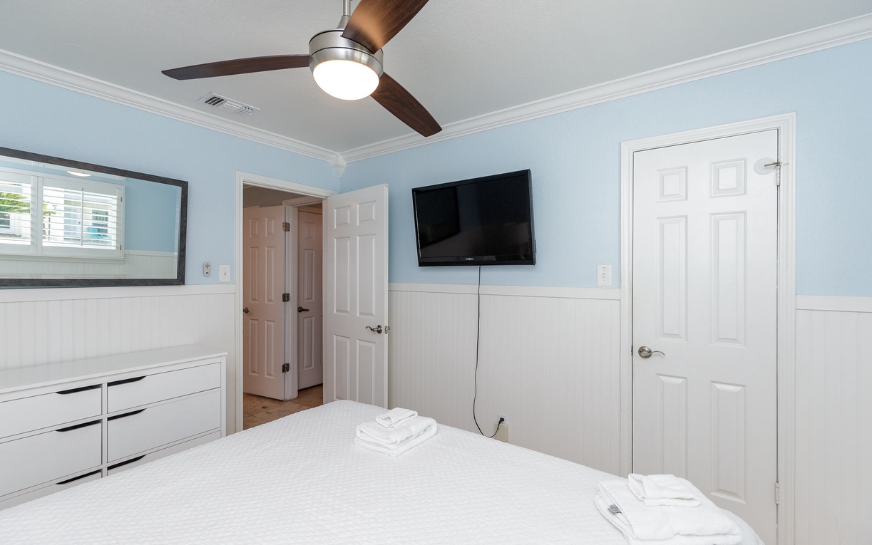 Relax in your peaceful bedroom with soft blue walls, modern ceiling fan, and wall-mounted TV for cozy nights in.