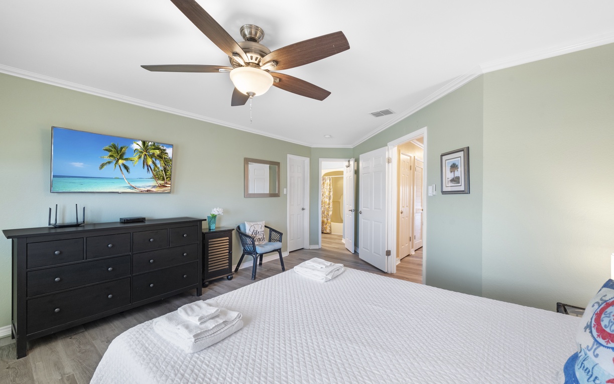 Relax in your peaceful bedroom with tropical ocean views on the wall-mounted TV and gentle ceiling fan creating perfect comfort.