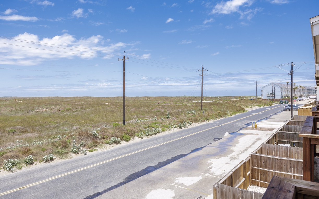 Coastal road stretches across natural dunes with power lines marking the surrounding area infrastructure.