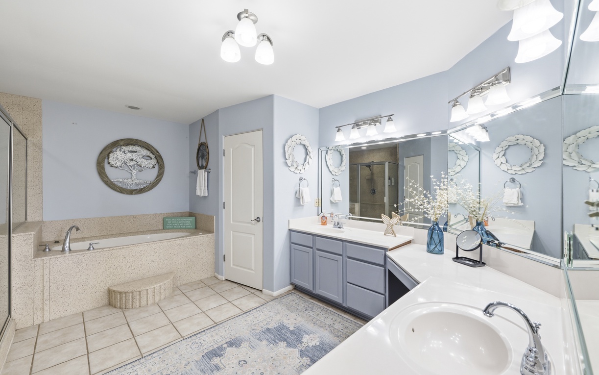 Primary bathroom with a tub, dual vanities, and plenty of natural light. The calming blue tones and beach-inspired decor create your perfect coastal retreat.