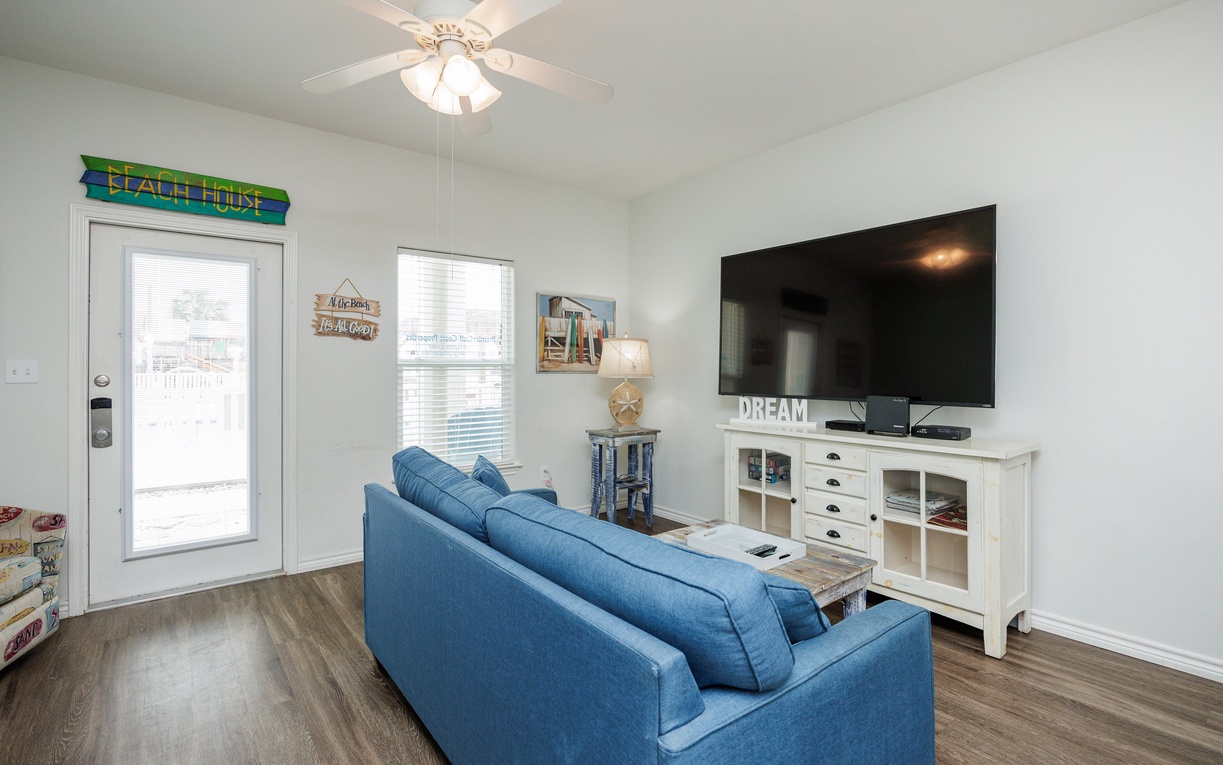 Unwind in your bright living room with comfortable blue seating, modern entertainment center, and peaceful views through large windows.