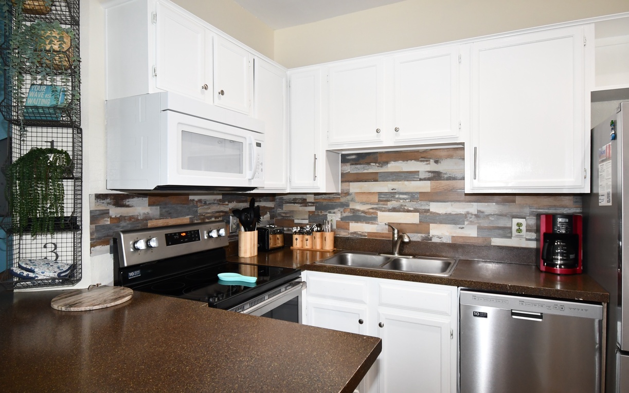 Your fully-equipped kitchen features gleaming white cabinetry, modern appliances, and a stunning wood-toned backsplash that adds warmth to your cooking space.