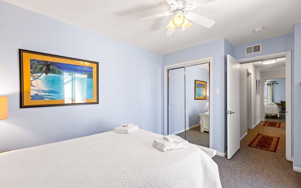 Unwind in your serene bedroom with soft blue walls and tropical artwork. Fresh linens await your arrival.
