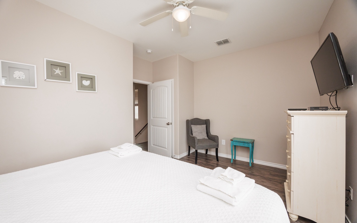 Unwind in your peaceful bedroom with plush white linens, ceiling fan, and flat-screen TV for cozy evenings.