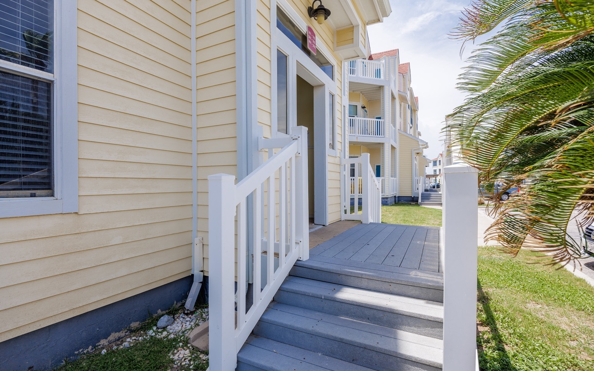 Coastal property entrance with wooden deck and palm trees creating a tropical welcome experience.