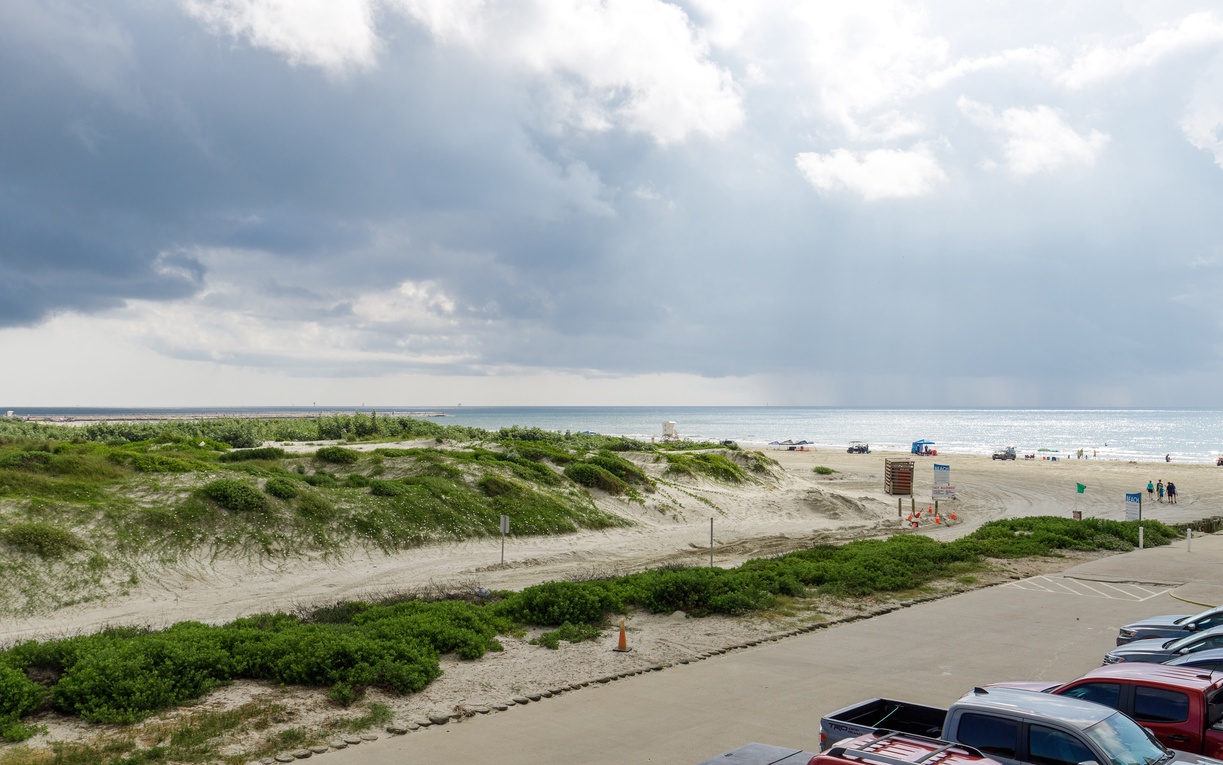 Expansive beachfront stretches along the coastline with convenient parking and natural dune vegetation framing the sandy shores.