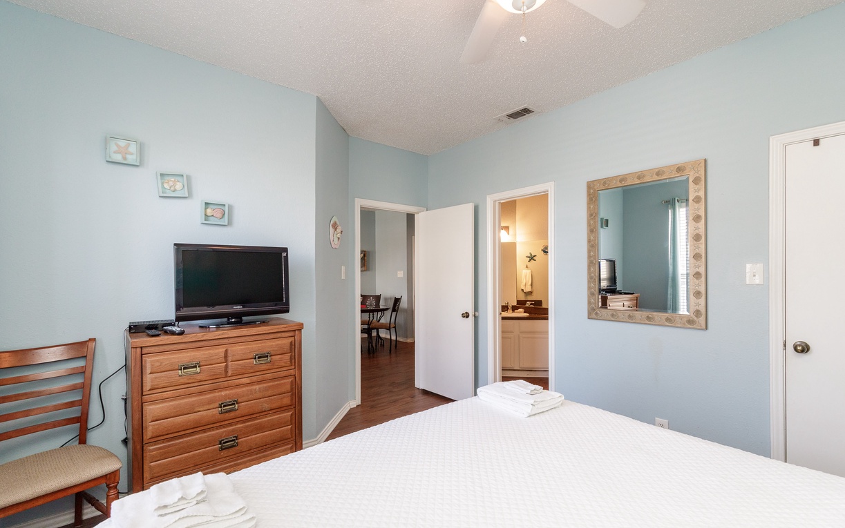 Relax in your peaceful bedroom with calming blue walls, comfortable furnishings, and thoughtful amenities including TV and private bathroom access.