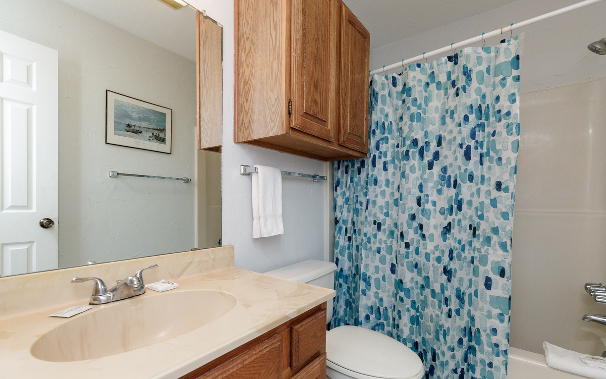 Step into your second floor guest bathroom with ocean-themed shower curtain and warm wood cabinetry for a coastal-inspired start to your day.