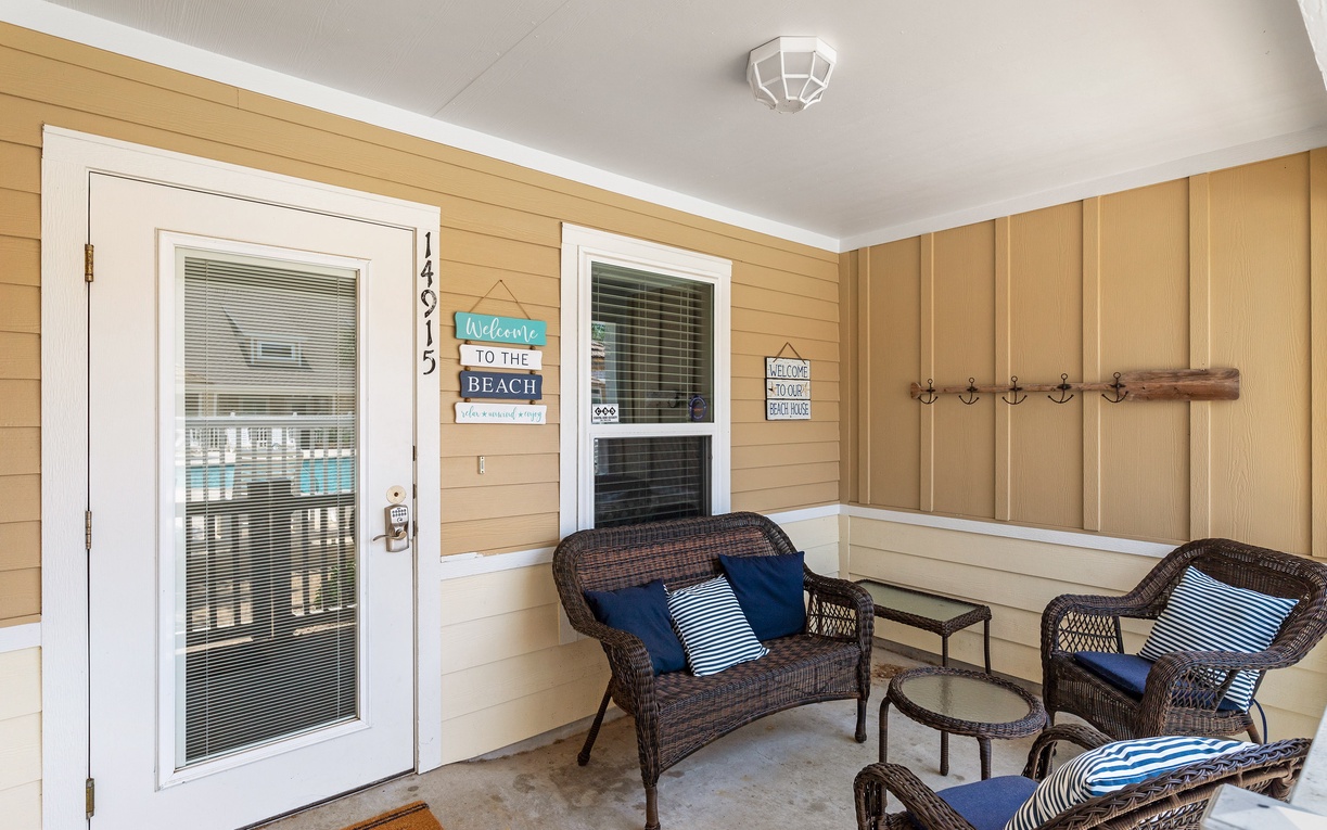 Your covered porch welcomes you with wicker seating and coastal charm, perfect for morning coffee or evening relaxation.